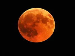 Ultra-realistic full moon during चंद्र ग्रहण (lunar eclipse) glowing behind mystical clouds, with temple silhouette in the foreground under a dark starry sky.